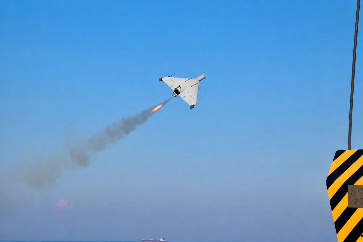White delta wing aircraft launches a rocket leaving an orange flame and smoke trail over a blue sea and clear sky