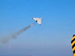 White delta wing aircraft launches a rocket leaving an orange flame and smoke trail over a blue sea and clear sky