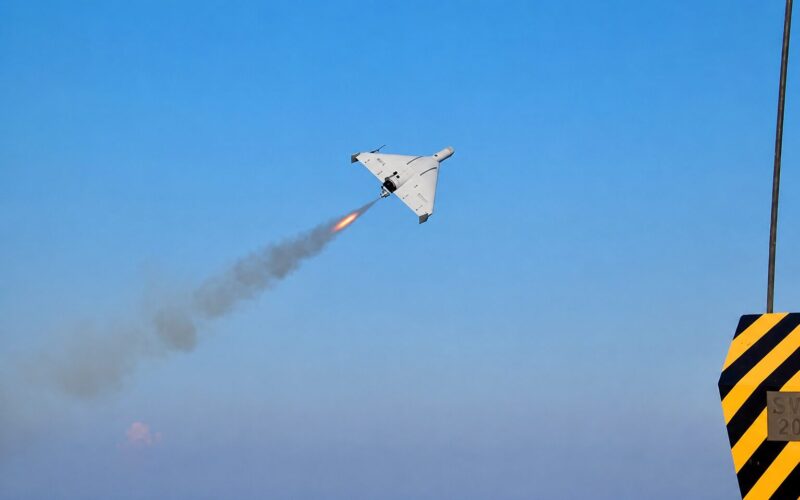 c621bc23 2c72 46b3 ba16 7a6e4f25812c White delta wing aircraft launches a rocket leaving an orange flame and smoke trail over a blue sea and clear sky