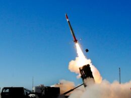 Missile launching from a ground launcher with a bright flame and smoke plume against a blue sky