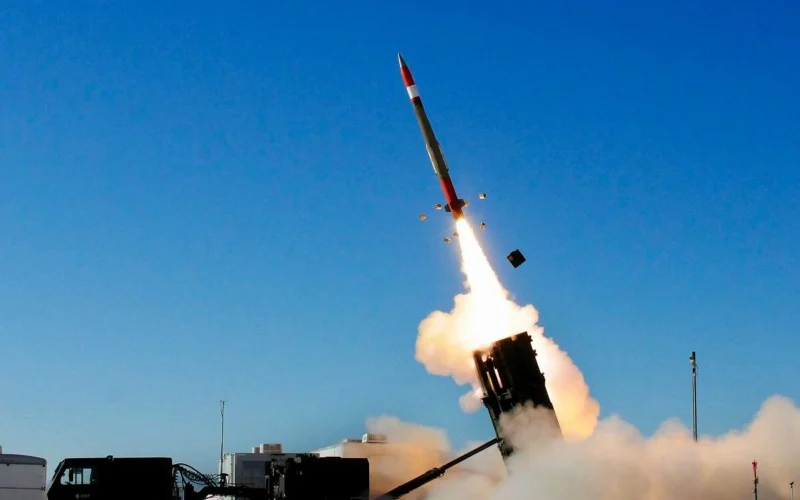 Missile launching from a ground launcher with a bright flame and smoke plume against a blue sky