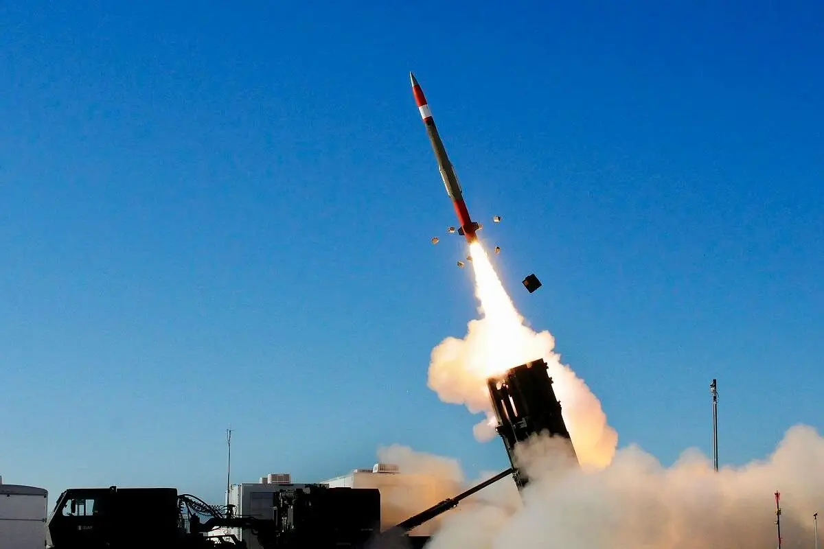 Missile launching from a ground launcher with a bright flame and smoke plume against a blue sky