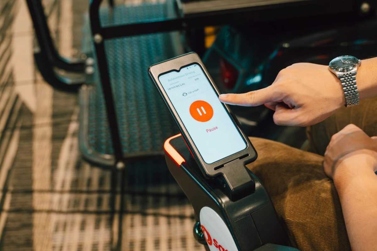 image Hand holding a phone mounted on a mobility scooter screen shows an autonomous driving app with a large orange pause button and Pause text
