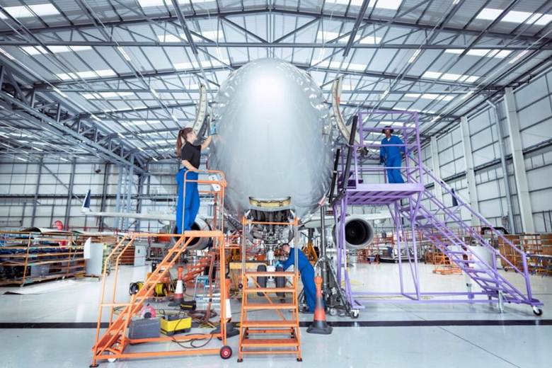 image Large aircraft nose cone undergoing assembly in a spacious hangar technicians in blue coveralls on orange and purple lifts working around it