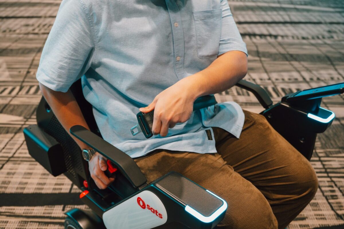 image Person wearing a light blue shirt sitting on an electric mobility scooter gripping the seat belt buckle near their lap