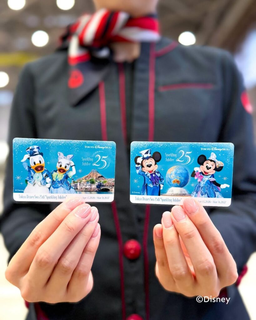 image Two blue Tokyo DisneySea 25th Sparkling Jubilee cards featuring Donald and Daisy on the left and a snowy backdrop held up by gloved hands in front of a person wearing a dark uniform with red piping