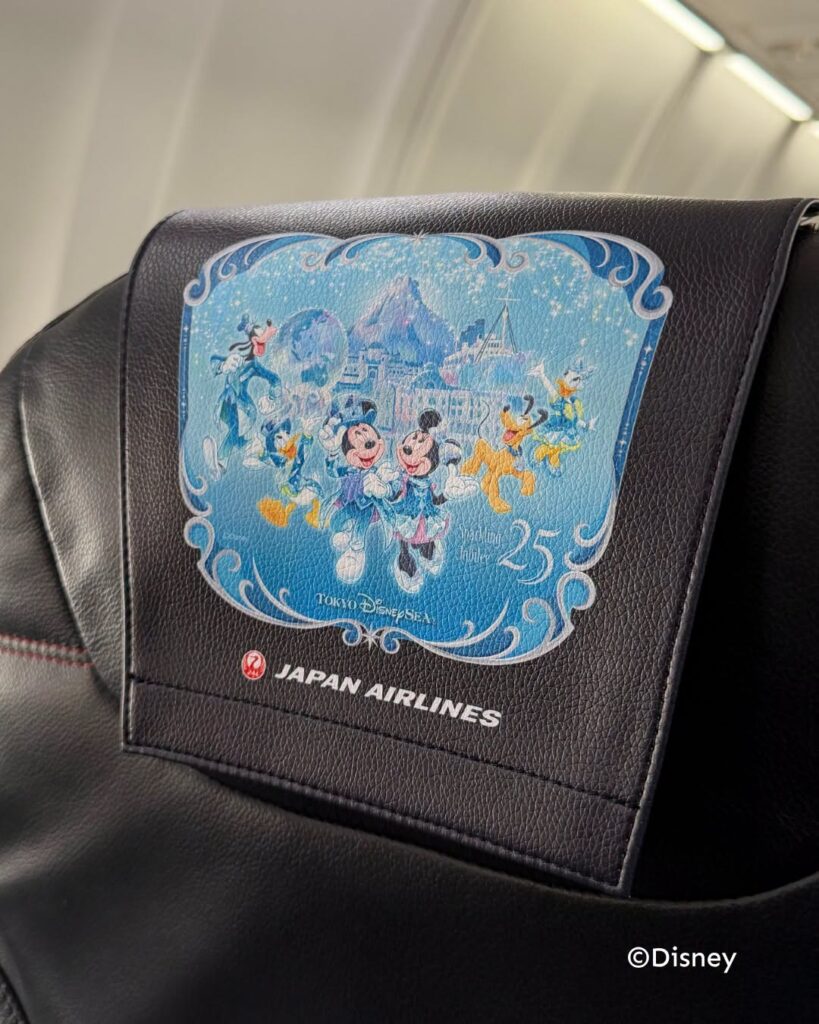 image Blue Tokyo DisneySea 25th anniversary design on a Japan Airlines seat headrest featuring Mickey Minnie and friends in a winter scene