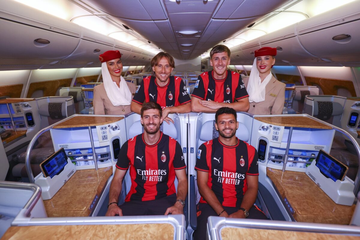 image AC Milan players in red and black jerseys posing with flight attendants inside a luxury airplane cabin