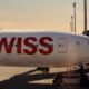 Swiss airplane at the gate nose to the right with bold red SWISS lettering on a white fuselage at sunset