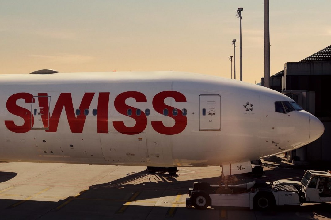 img Swiss airplane at the gate nose to the right with bold red SWISS lettering on a white fuselage at sunset