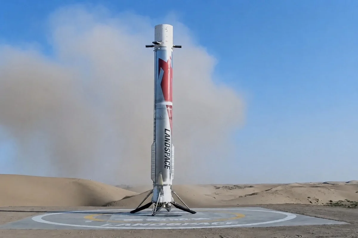 landspace Silver rocket standing upright on a circular landing pad in a desert with blue sky above
