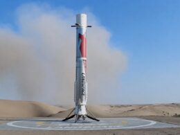 Silver rocket standing upright on a circular landing pad in a desert with blue sky above