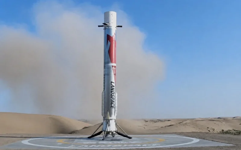 Silver rocket standing upright on a circular landing pad in a desert with blue sky above