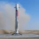 Silver rocket standing upright on a circular landing pad in a desert with blue sky above