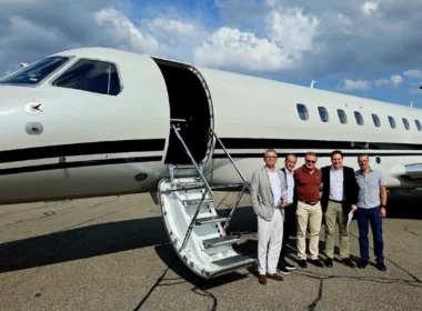Five men in smart casual attire pose beside a white private jet with its door open and a portable staircase on the tarmac