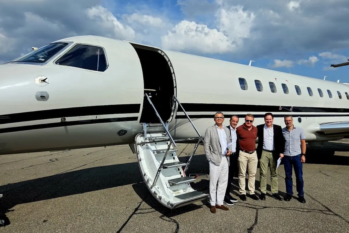 peakjet first flight Five men in smart casual attire pose beside a white private jet with its door open and a portable staircase on the tarmac