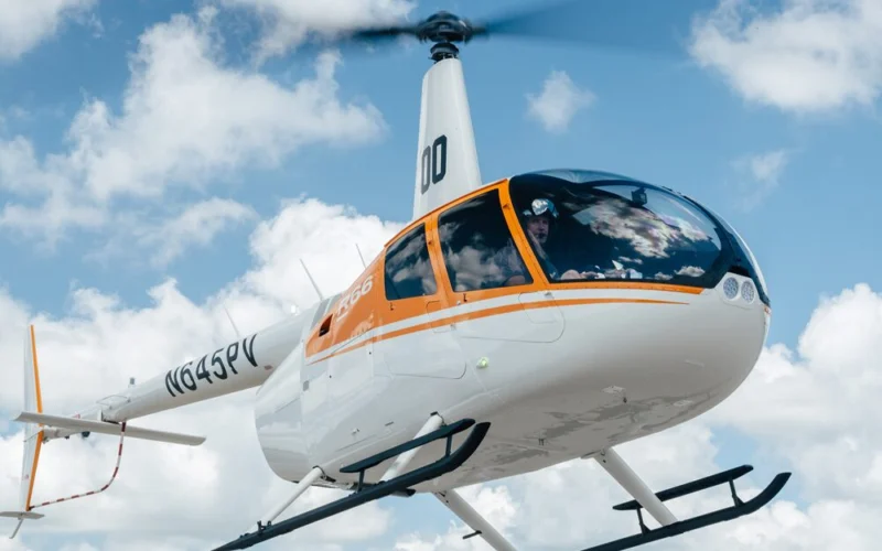 White helicopter with an orange stripe flying in a clear blue sky with scattered clouds