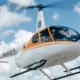 White helicopter with an orange stripe flying in a clear blue sky with scattered clouds