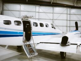 Inside a hangar a white private jet with blue stripes and an open door with a portable staircase attached