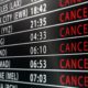 Flight status board showing multiple flights with many as CANCELLED red across routes like Los Angeles New York City Toronto Paris Tokyo Madrid etc