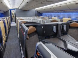 Interior of a modern airplane in business class showing private lie flat seats and partitioned pods with blue ambient lighting facing forward