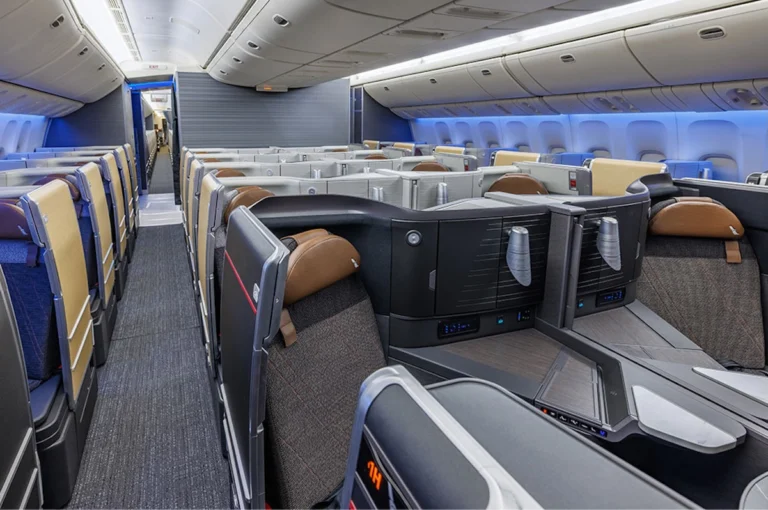 Interior of a modern airplane in business class showing private lie flat seats and partitioned pods with blue ambient lighting facing forward