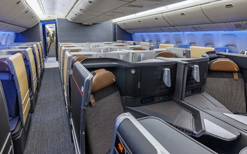 Interior of a modern airplane in business class showing private lie flat seats and partitioned pods with blue ambient lighting facing forward