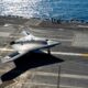 A gray F 35B stealth jet on the deck of an aircraft carrier with the ocean in the background