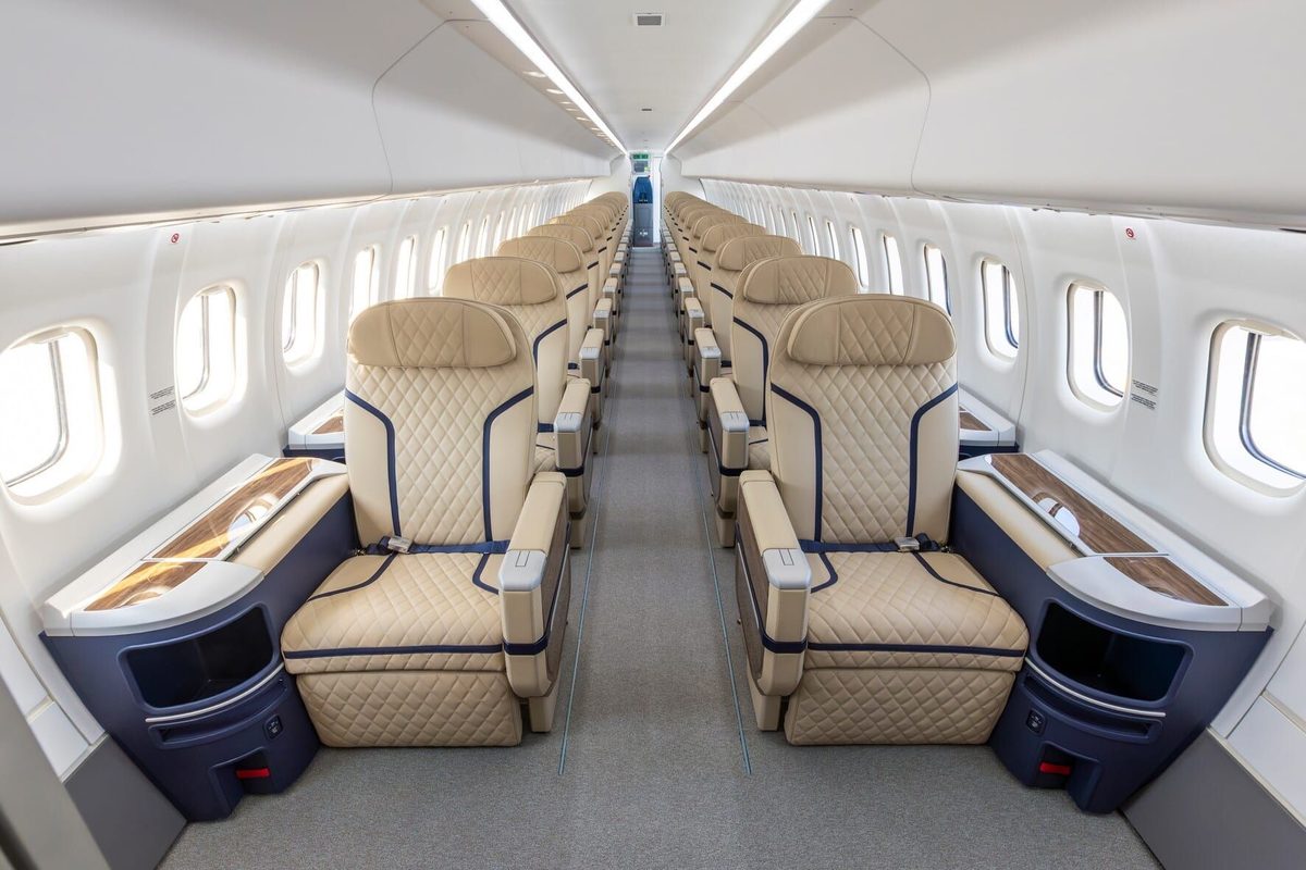 1779401309130 Aisle view of an empty aircraft cabin with beige quilted seats and woodtrim tables on the sides of the aisle