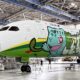 Airliner inside a maintenance hangar with a bright green and blue cartoon dragon mural along the fuselage