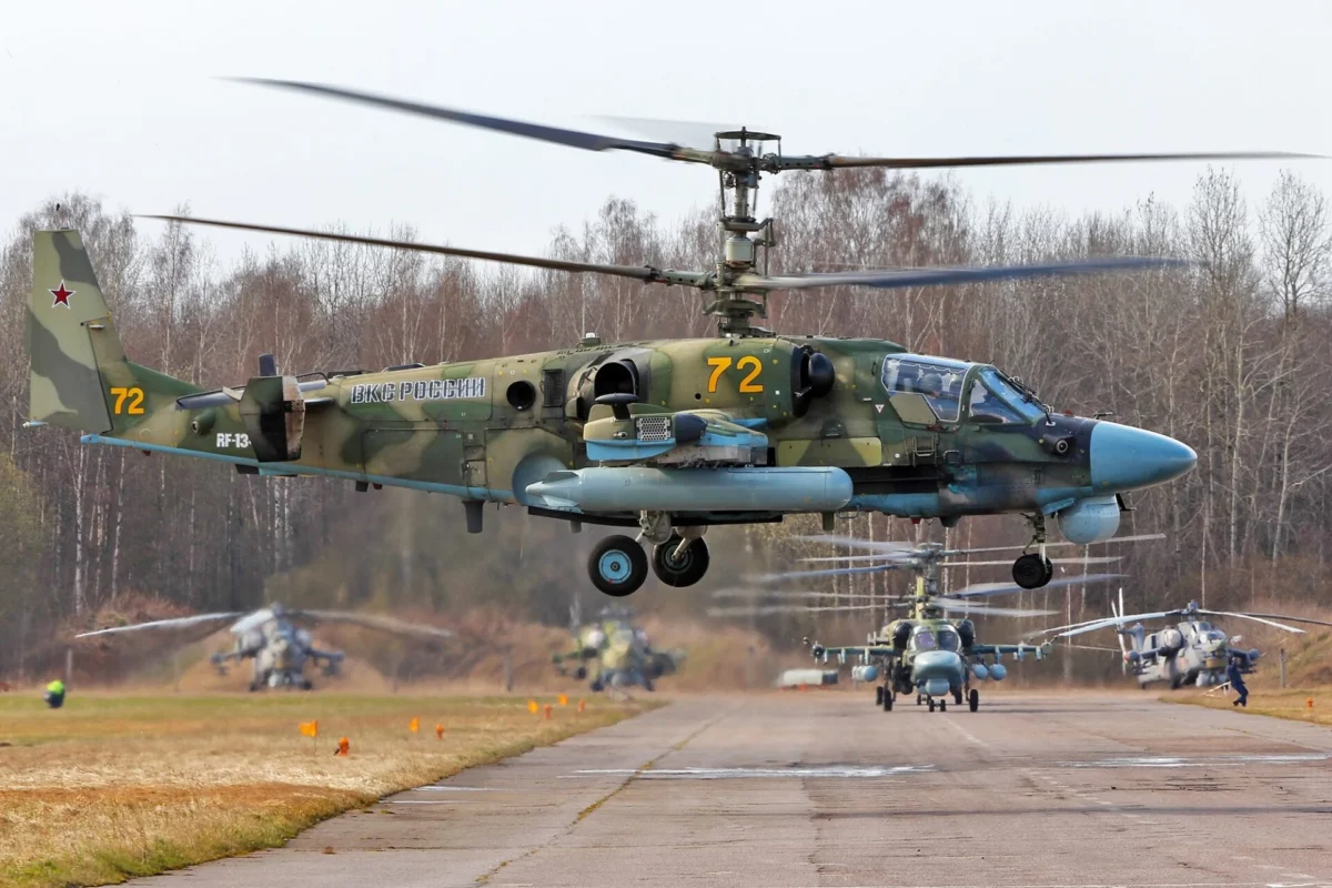 A Russian Ka 52 Alligator attack helicopter hovers above an airfield with other Ka 52 and Mi 28 helicopters in the background A Russian Ka 52 Alligator attack helicopter hovers above an airfield with other Ka 52 and Mi 28 helicopters in the background
