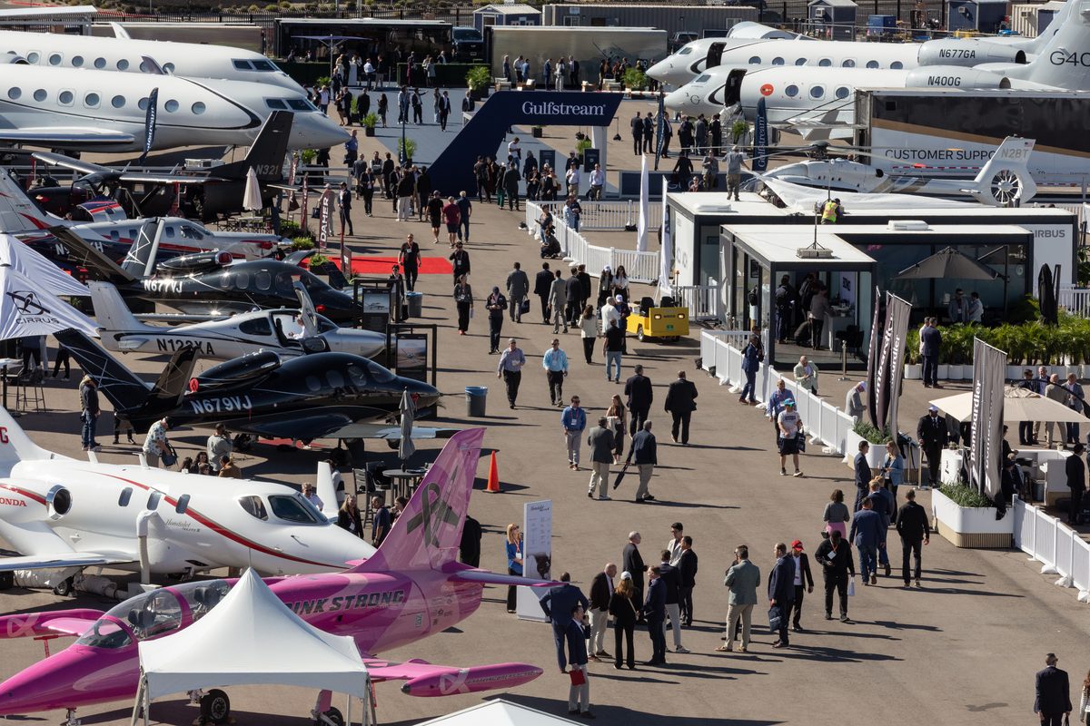 Aircraft Connection Aerial View Busy aircraft expo with private jets parked on both sides and visitors walking along a central aisle under a Gulfstream banner signage
