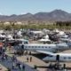 Air show at an airport with numerous private jets tents and attendees set against desert mountains in the distance