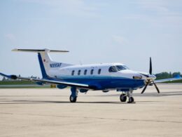 Blue and white twin engine propeller aircraft parked on a sunlit airport tarmac registration N995AF