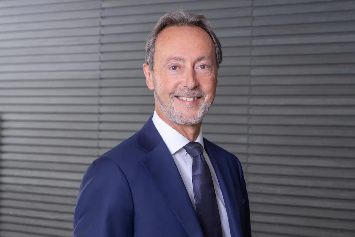 Fabrice Brégier final Professional headshot smiling man in a navy suit and purple tie against a gray striped backdrop