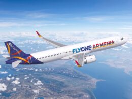 White passenger jet with FlyOne Armenia livery flying above clouds and coastline at altitude