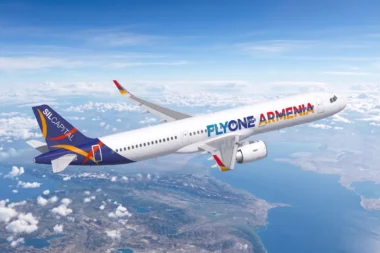 White passenger jet with FlyOne Armenia livery flying above clouds and coastline at altitude