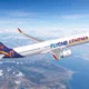 White passenger jet with FlyOne Armenia livery flying above clouds and coastline at altitude