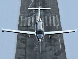 Small airplane viewed from above landing on a runway surrounded by blue gray surface lines and markings ahead of it
