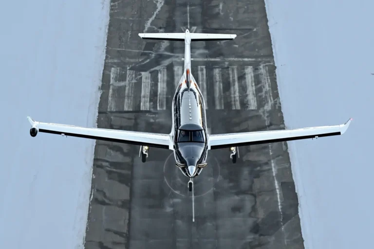 Small airplane viewed from above landing on a runway surrounded by blue gray surface lines and markings ahead of it