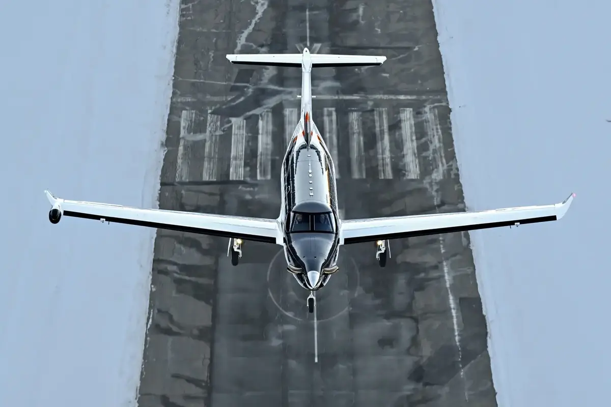 Pilatus PC 12 PRO 1200x800 Small airplane viewed from above landing on a runway surrounded by blue gray surface lines and markings ahead of it