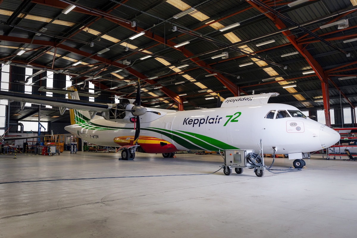 Prototype Kepplair 72©KepplairEvolution Twinturboprop passenger plane in a large maintenance hangar white fuselage with green stripes and a colorful tail Nearby ground support equipment visible