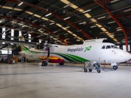 Twinturboprop passenger plane in a large maintenance hangar white fuselage with green stripes and a colorful tail Nearby ground support equipment visible