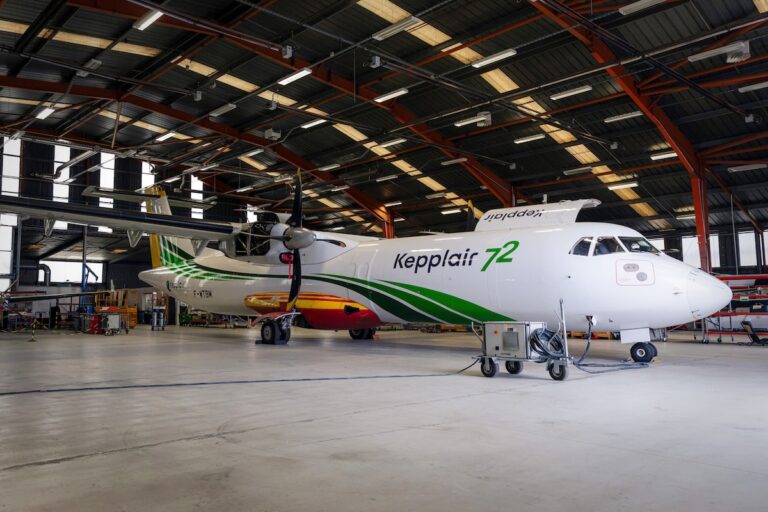 Twinturboprop passenger plane in a large maintenance hangar white fuselage with green stripes and a colorful tail Nearby ground support equipment visible