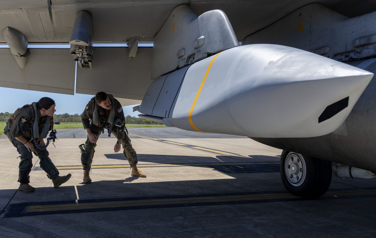 JASSM ER Two pilots in flight suits crouch under a large military aircraft wing inspecting the underwing equipment on the tarmac