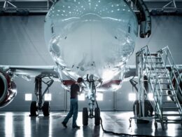 Technician inspecting the nose of a large jet in a hangar with mobile stairs nearby during maintenance