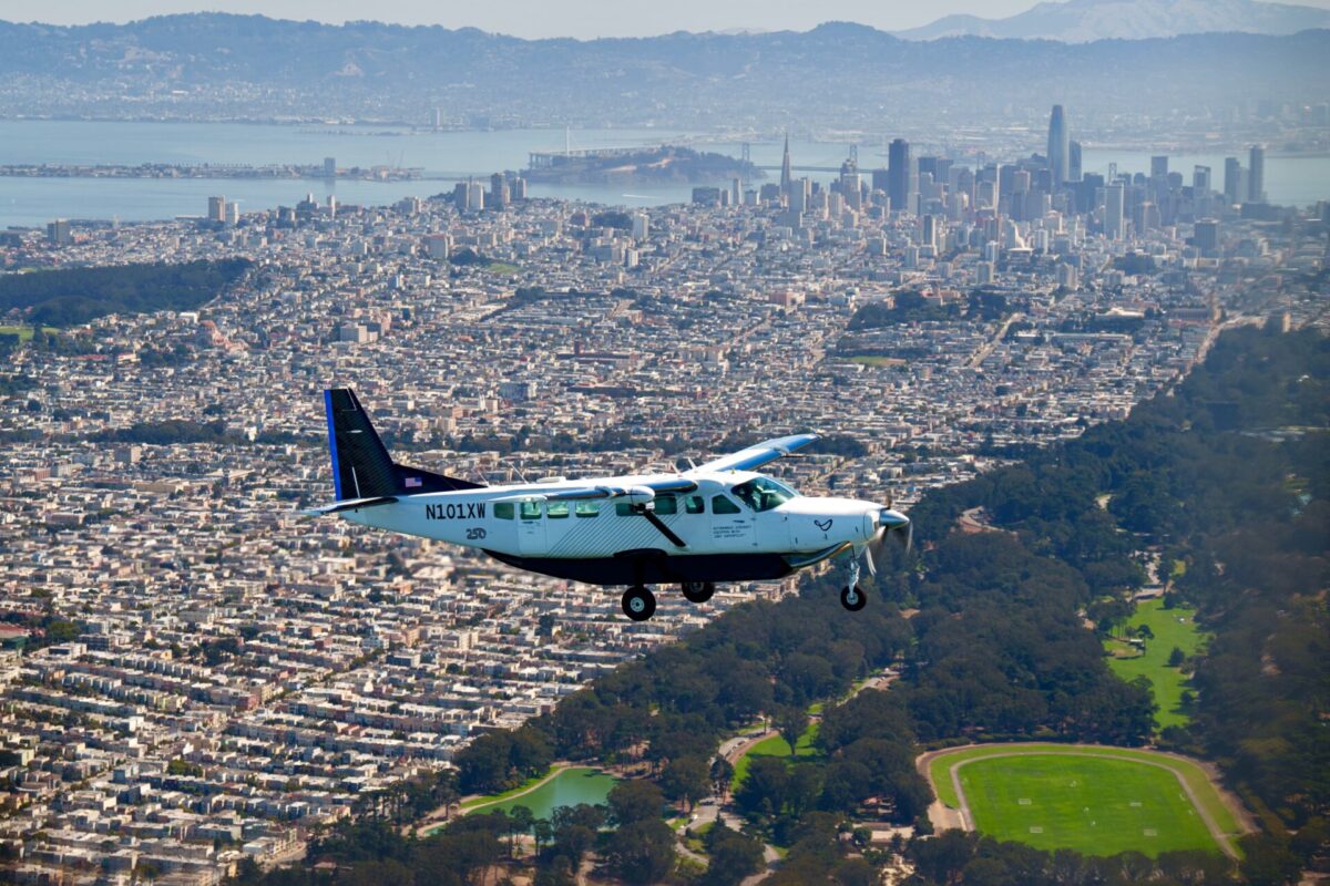 Recently Saved 1 of 1 11 Small white and blue aircraft flying low over a densely built city with hills and a bay in the background