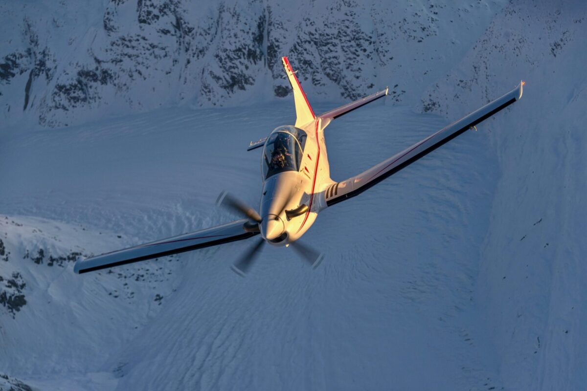 Recently Saved 1 of 1 White single engine airplane banking over a snow covered mountain landscape at sunset