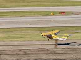 Small yellow biplane lifting off the runway tail marked ELECTRA and registration N301EL