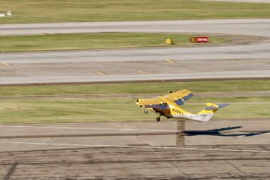 Small yellow biplane lifting off the runway tail marked ELECTRA and registration N301EL